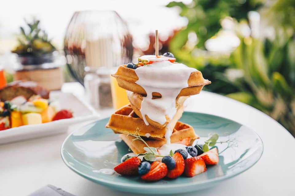 Gourmet waffle stack with whipped cream, berries, and fruit on turquoise plate outdoors