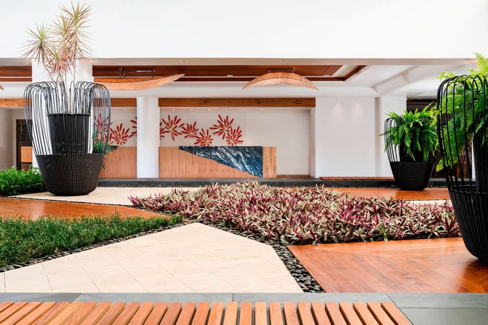 Modern resort lobby with wooden beams, tropical plants, and contemporary design elements