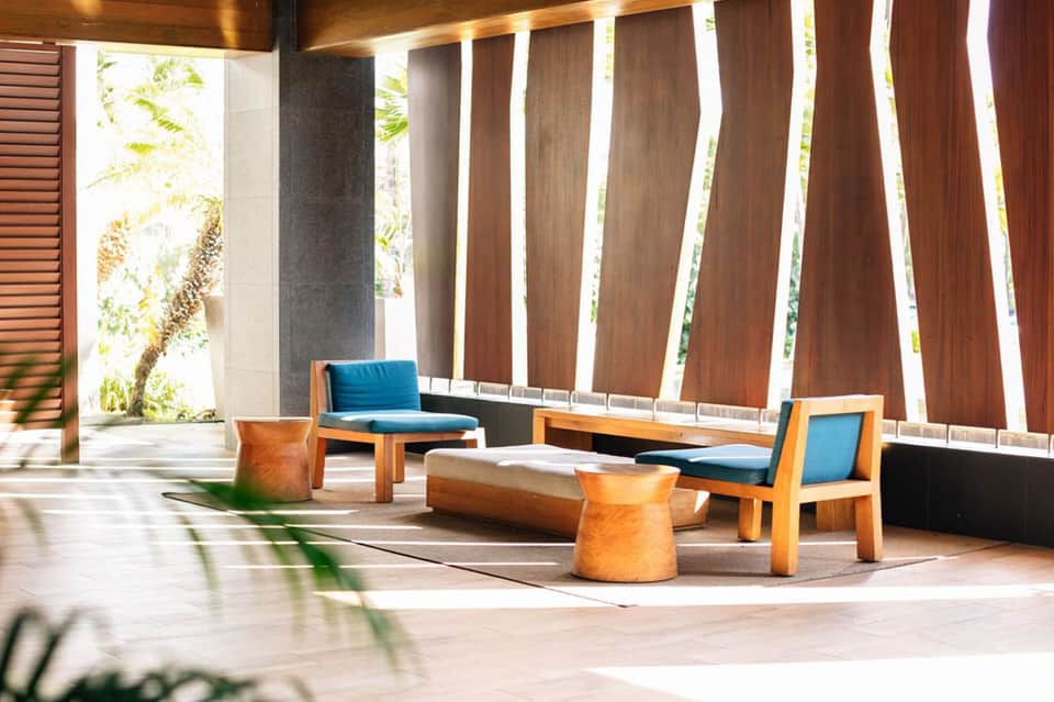 Contemporary lounge with wooden slat wall, blue cushioned seating, and tropical views
