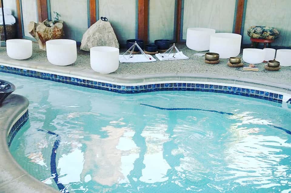 Indoor swimming pool with white singing bowls and meditation instruments displayed on deck