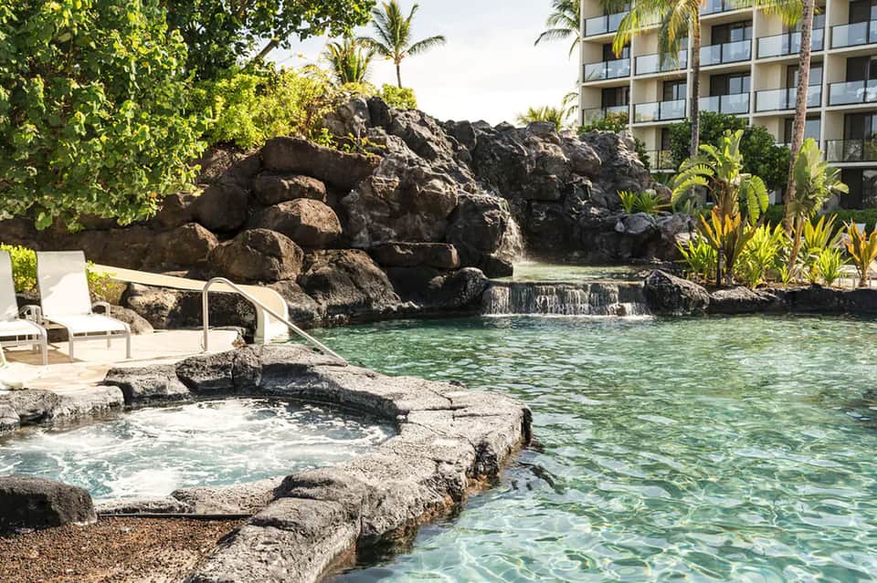 Scenic resort lagoon pool with natural rock formations, waterfall, and tropical vegetation