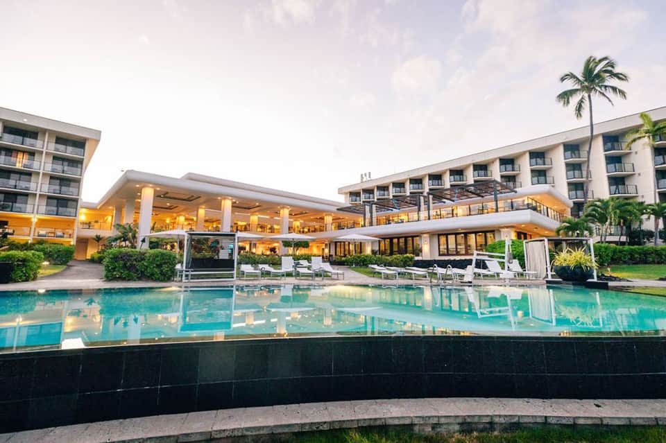 Modern resort exterior at dusk with illuminated buildings and turquoise pool