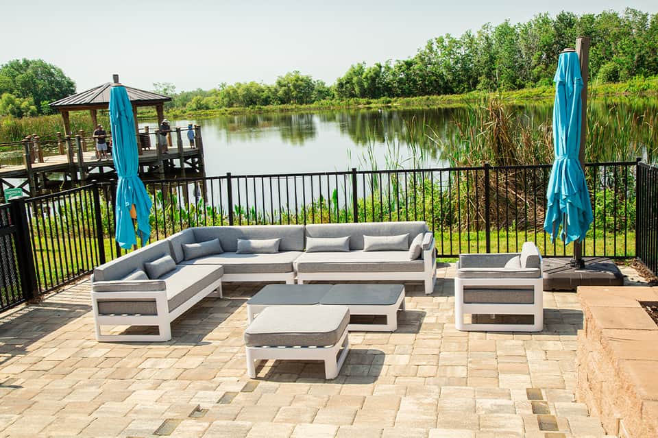 Waterfront deck with white seating, blue umbrellas, railing, and marshland view