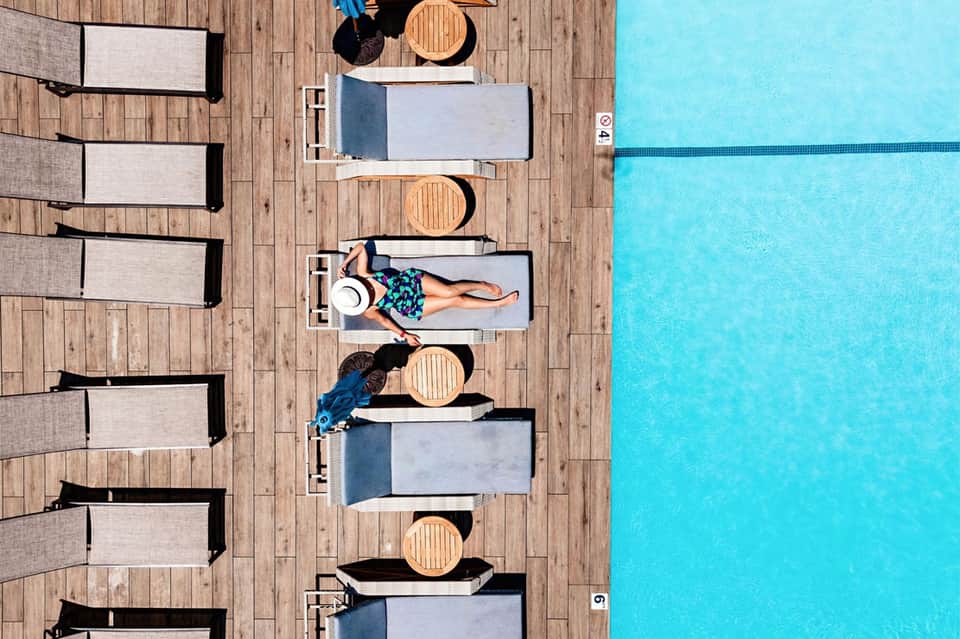 Aerial view of swimming pool deck with lounge chairs and sunbathers on wooden platform