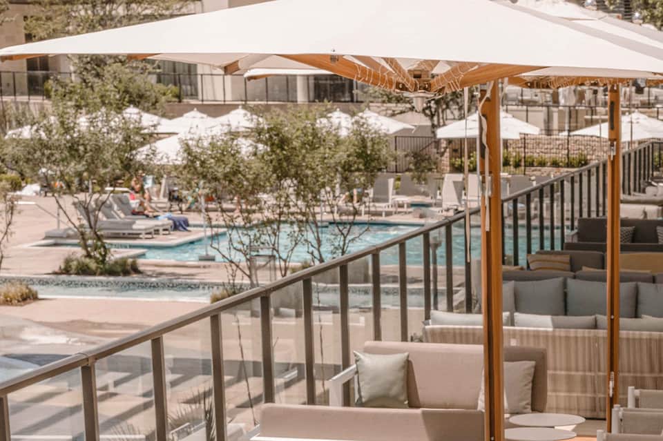 Outdoor terrace with shaded seating overlooking resort pool and grounds with umbrellas