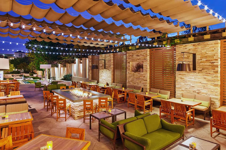 Evening patio lounge with fire pit, string lights, and blue-toned canopy overhead