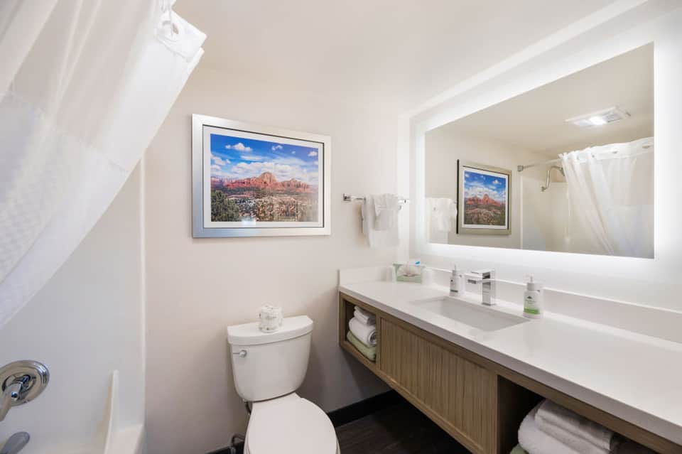 Clean modern bathroom with dual sink vanity, large illuminated mirror, and landscape artwork