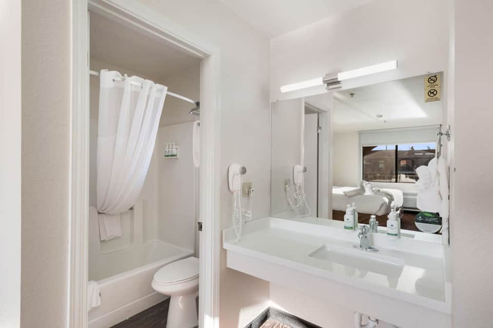 Clean hotel bathroom with white vanity, mirror, shower, and toilet