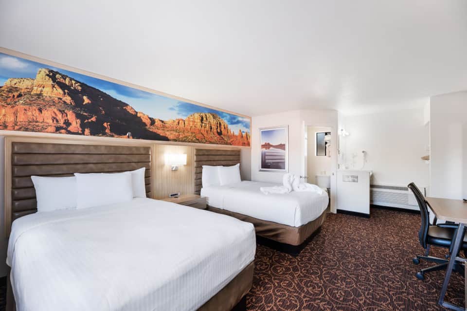 Hotel room with two queen beds and desert landscape artwork above headboards