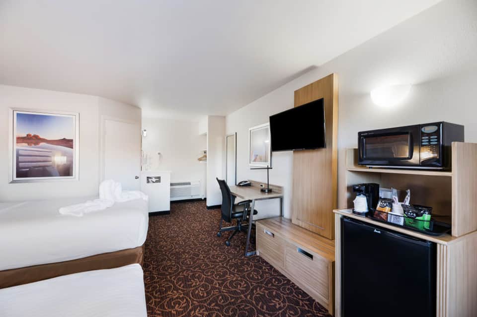 Hotel room with two queen beds, desk with TV, microwave, and brown patterned carpet