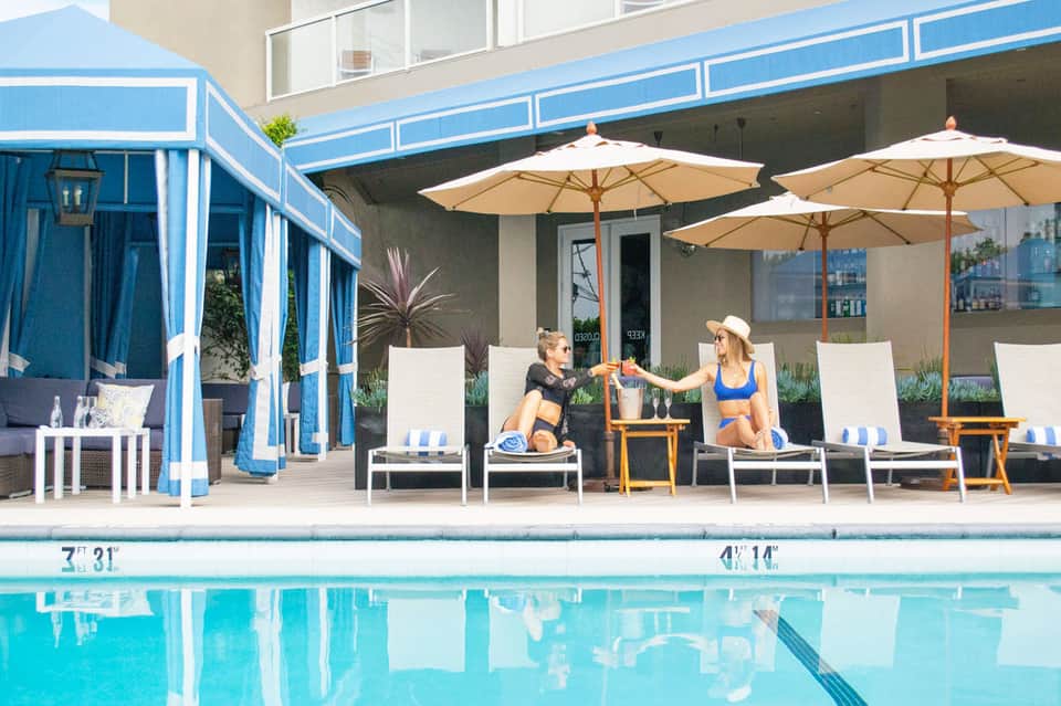 Resort poolside with lounge chairs, umbrellas, and two guests relaxing by the blue pool
