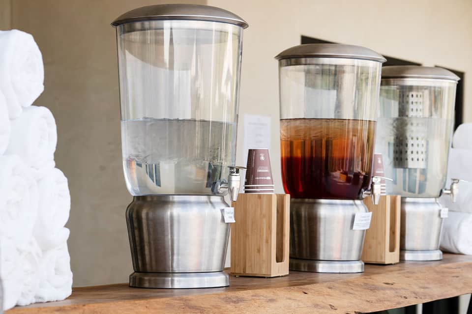 Beverage dispensers with water and iced tea on wooden counter with white towels