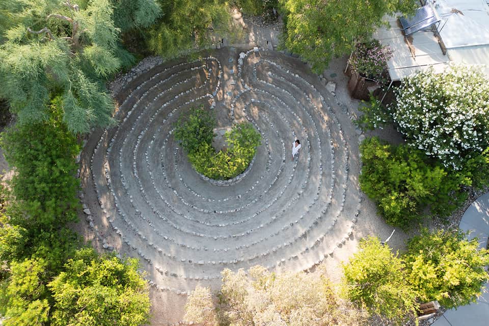 Aerial view of spiral stone labyrinth pathway surrounded by lush green landscaping