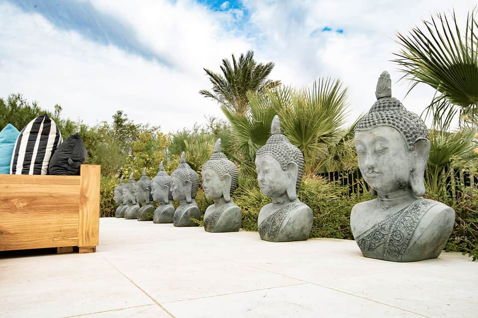 Garden display with stone Buddha head sculptures, palm trees, and decorative wooden surf board