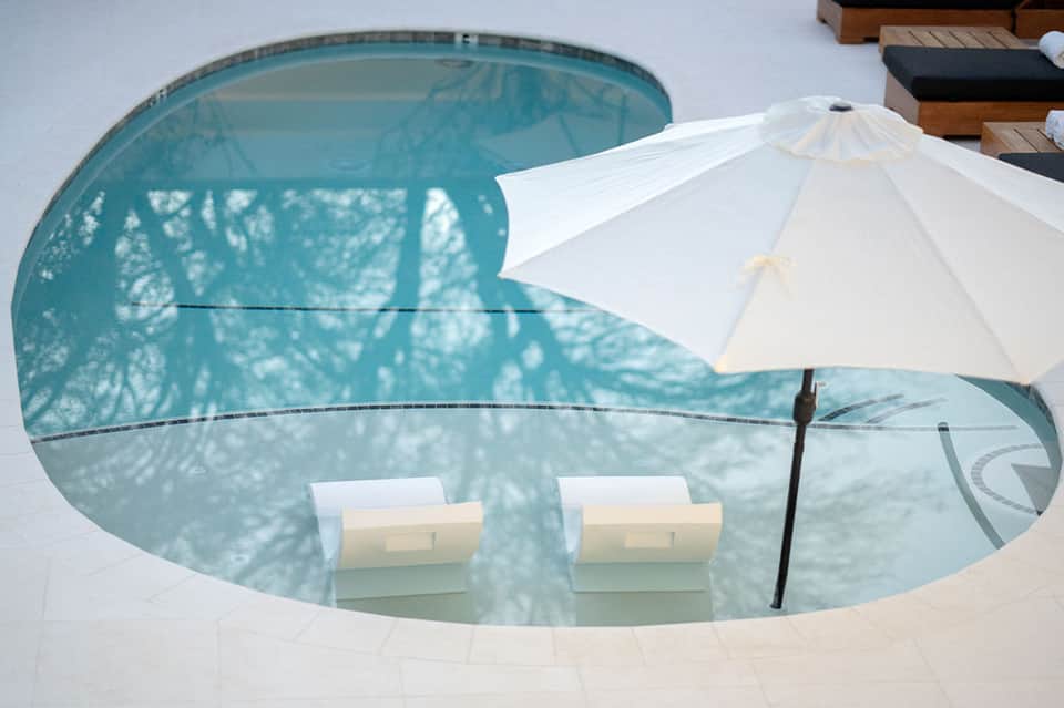 Small curved pool with white umbrellas and lounge chairs in minimalist resort setting