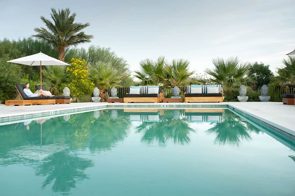 Luxury resort pool reflecting palm trees with lounge seating areas and white umbrellas