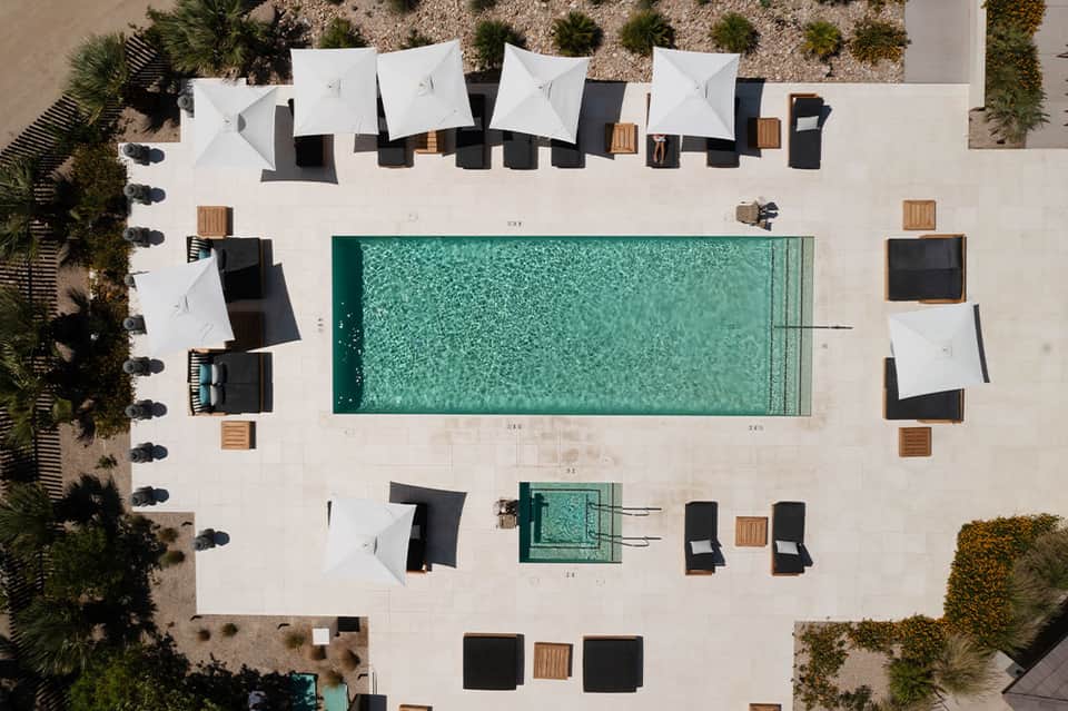 Aerial view of resort pool deck with white umbrellas, black loungers, and green landscaping