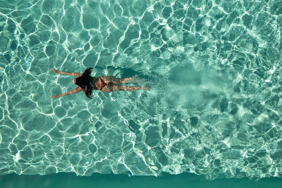 Aerial view of woman snorkeling in crystal clear turquoise shallow water with visible sandy bottom