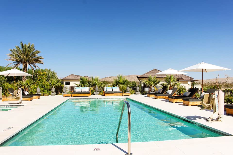 Resort lap pool with turquoise water, lounge chairs, white umbrellas, and mountain desert backdrop