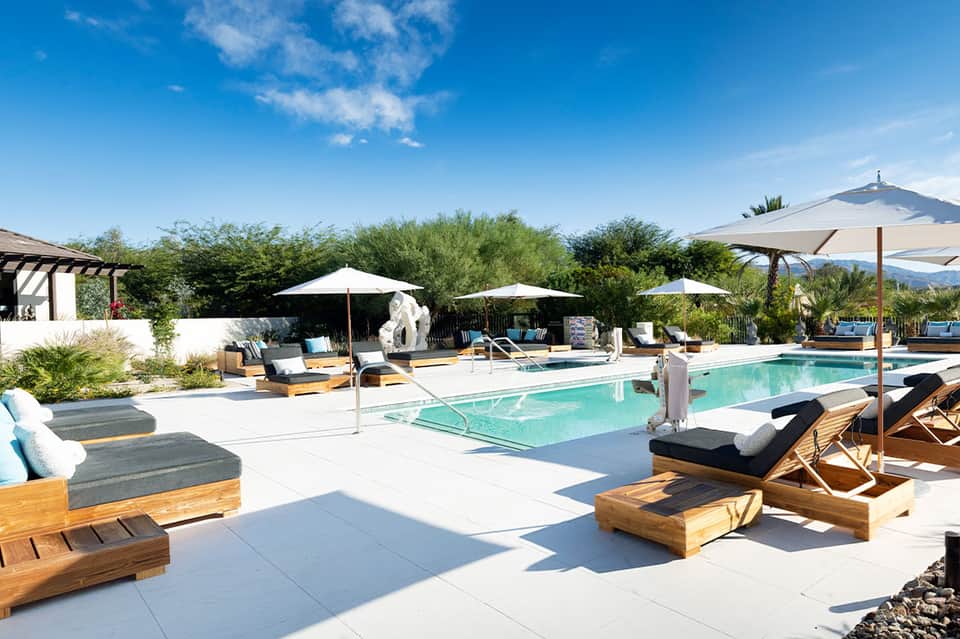 Desert resort pool area with lounge chairs, umbrellas, and mountain backdrop