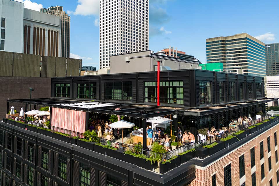 Urban rooftop venue with black modern building, outdoor seating, umbrellas, and city skyline