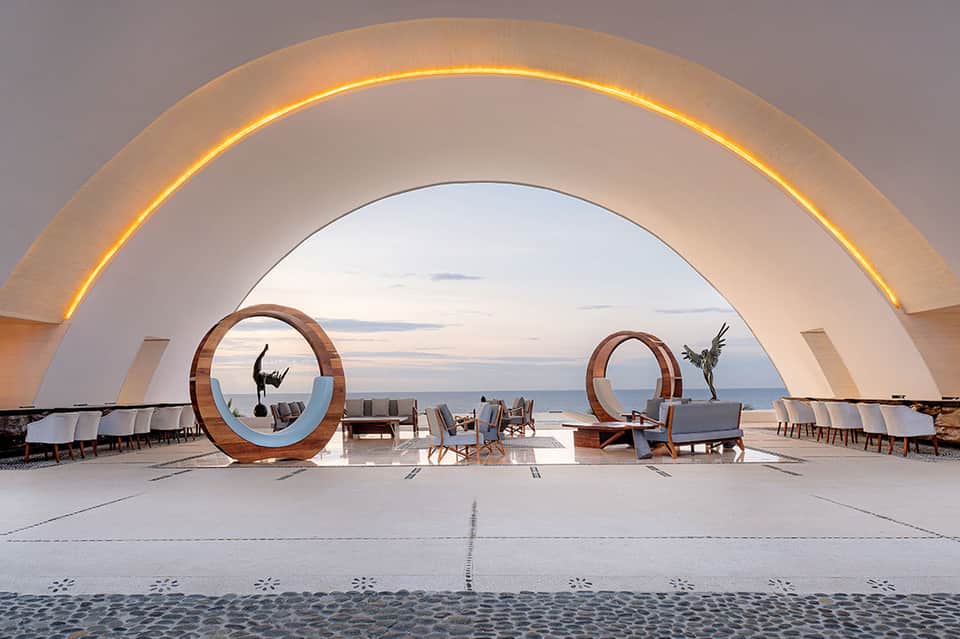 Modern beachfront architecture with illuminated white arch, sculpture circles, loungers, and ocean