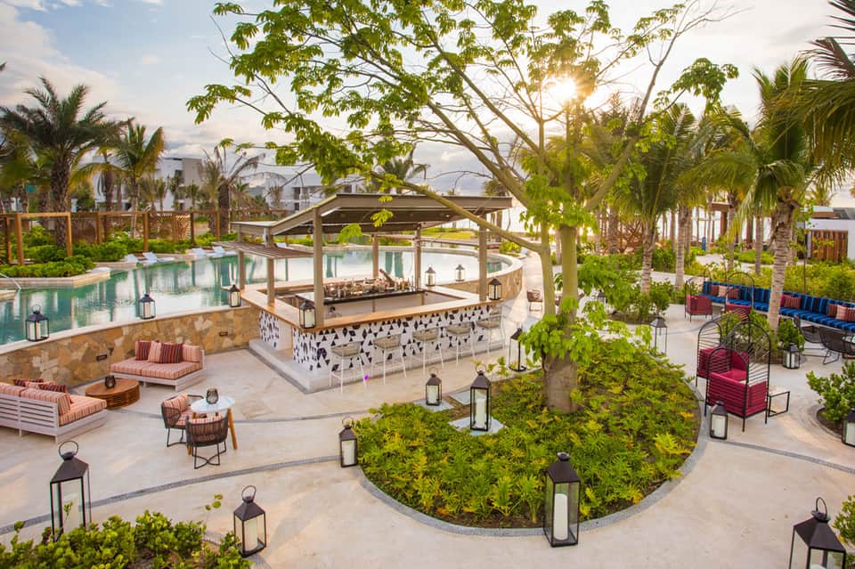 Expansive resort courtyard featuring lagoon pool, bar, tropical landscaping, loungers, and palm trees at sunset