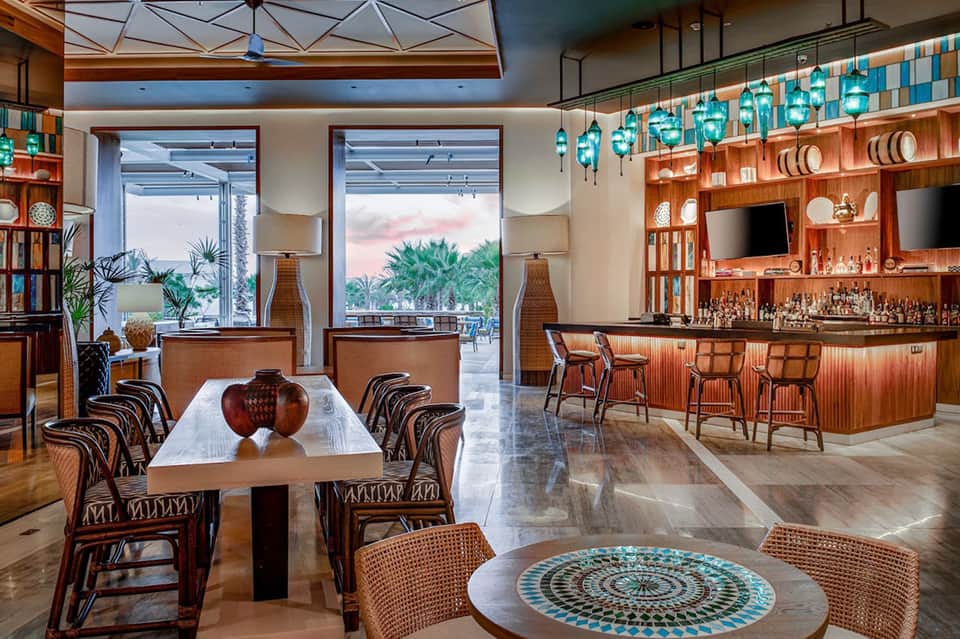 Modern resort bar and lounge with wooden design, turquoise pendant lights, and ocean views