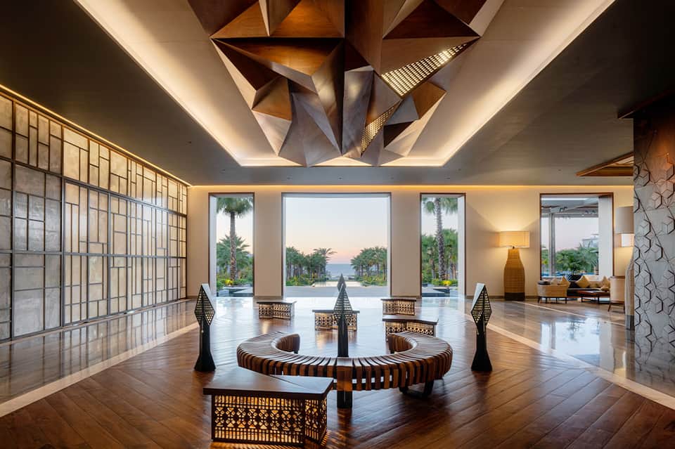 Modern resort lobby with geometric ceiling sculpture and ocean view through columns