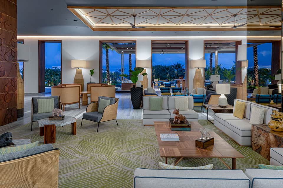 Elegant resort lobby with seating areas, large windows with palm tree views, and modern furnishings