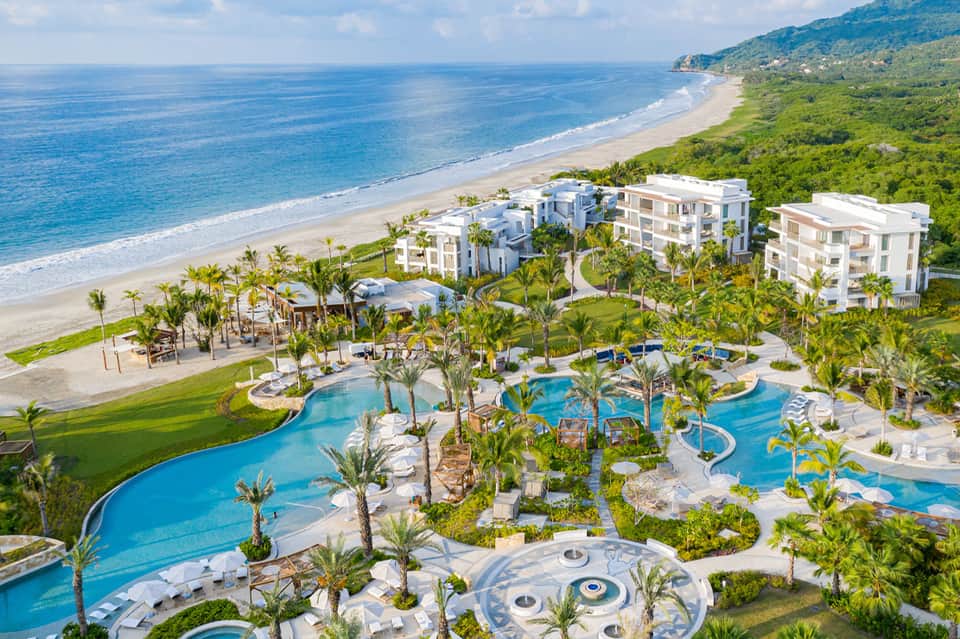 Aerial view of beachfront resort with pools, palm trees, and pristine sandy beach
