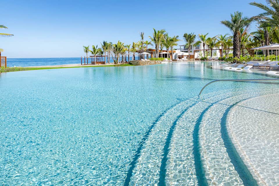 Resort lagoon pool with crystal clear turquoise water, palm trees, and beachfront cabanas