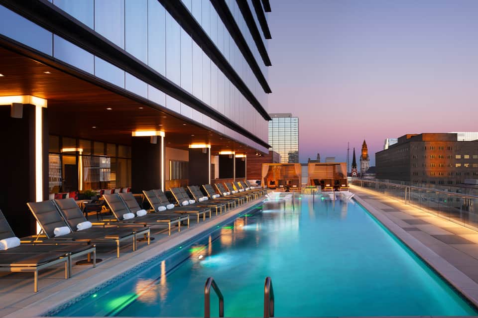 Modern rooftop pool at dusk with lounge chairs, city skyline, and ambient lighting