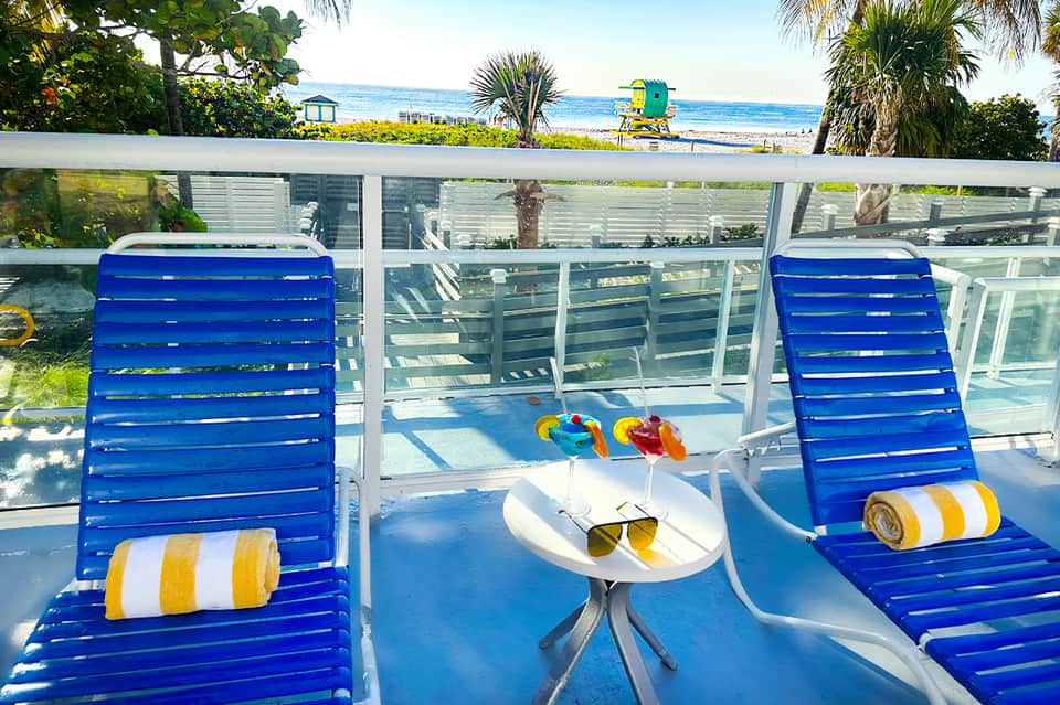 Two blue beach chairs with white side table overlooking ocean and sandy beach