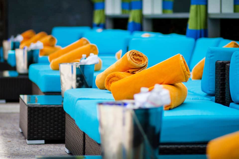 Blue lounge chairs with rolled orange towels and white pillows arranged on a patio