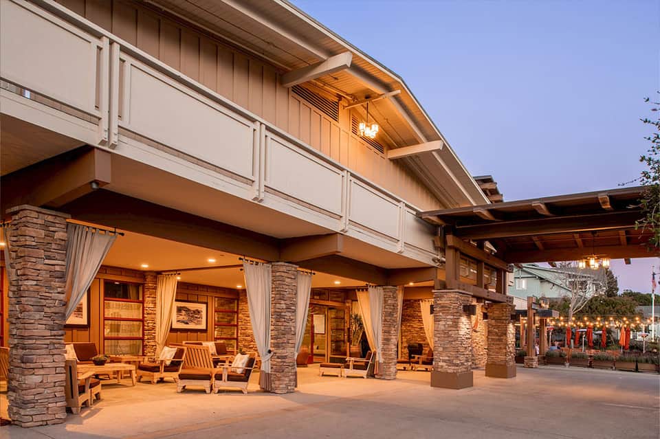 Modern building exterior at dusk with illuminated columns, stone facade, and covered lounge area
