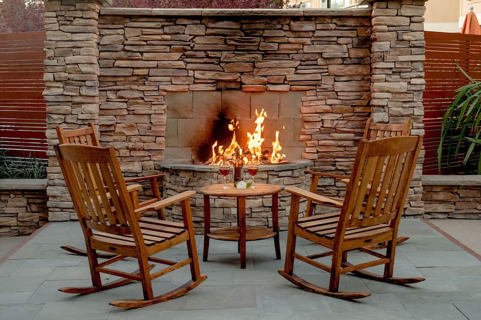 Outdoor fireplace with stone surround and wooden rocking chairs on patio seating area