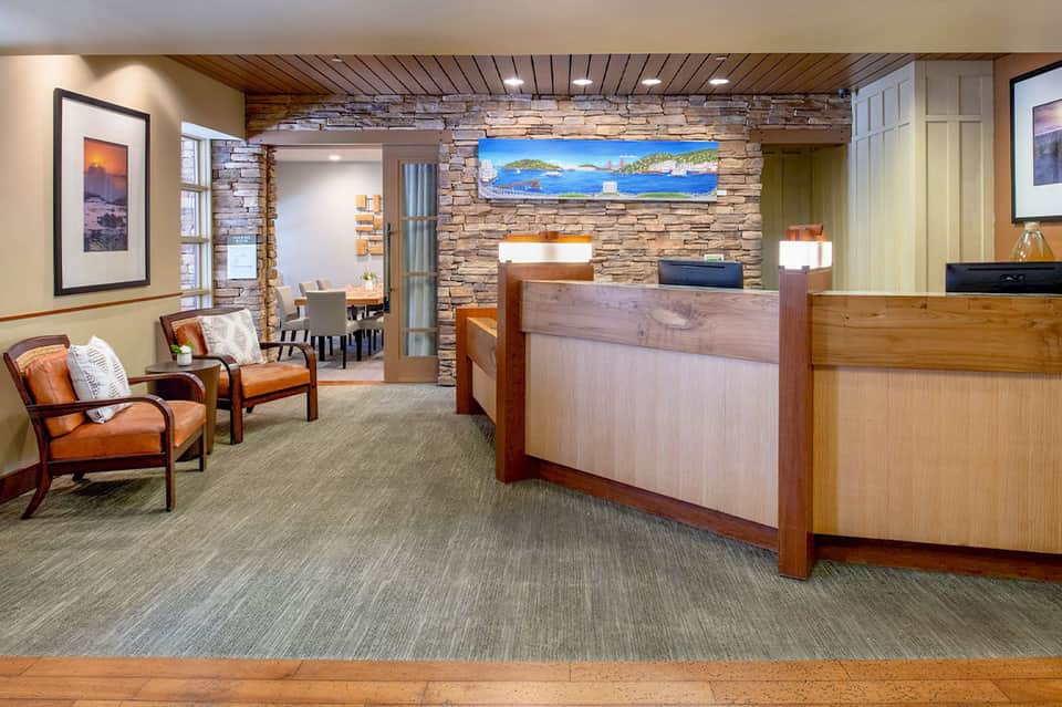 Hotel lobby interior with stone fireplace accent wall, wooden reception desk, leather seating, and coastal artwork