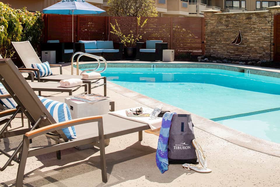 Resort pool deck with lounge chairs, striped umbrellas, privacy fence, and lush landscaping