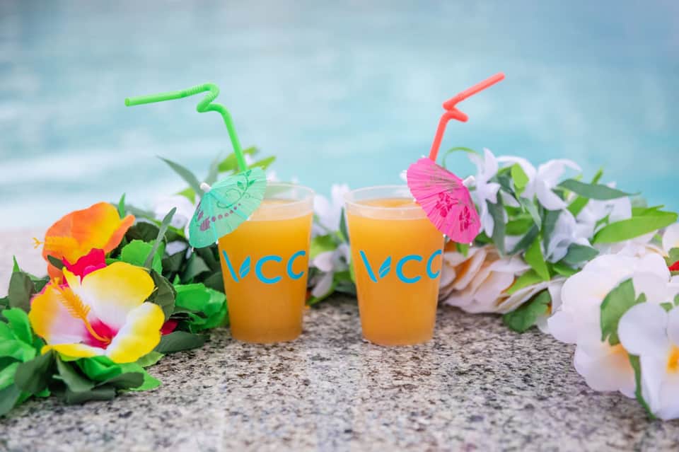 Two tropical juice drinks with colorful umbrellas and straws surrounded by vibrant flowers