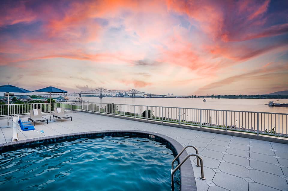Resort pool deck at sunset with ocean bridge view, lounge chairs, and dramatic pink sky
