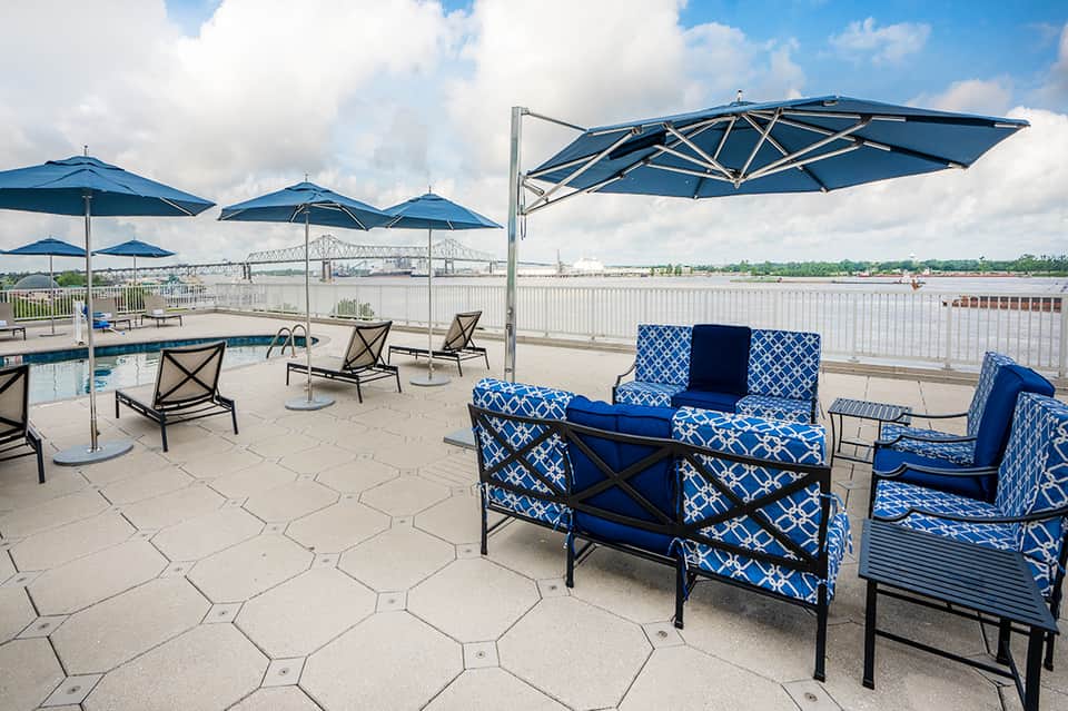 Waterfront patio with blue umbrellas, patterned seating, and river bridge view