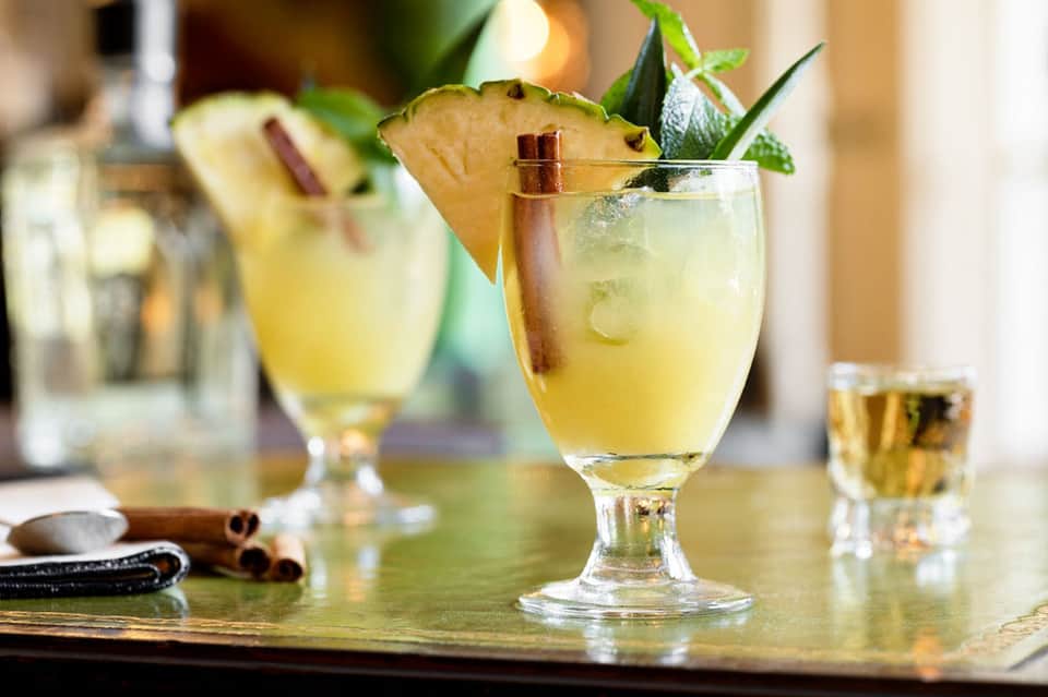 Cocktails with pineapple garnish, mint leaves, and cinnamon sticks on bar counter