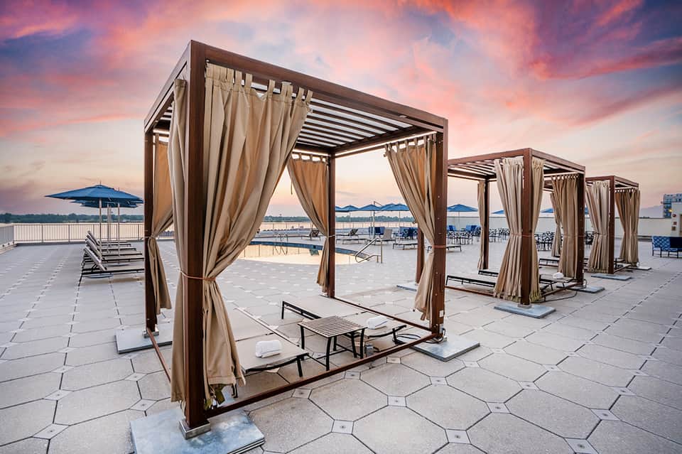 Waterfront deck with rows of modern cabanas featuring draped curtains at golden hour sunset