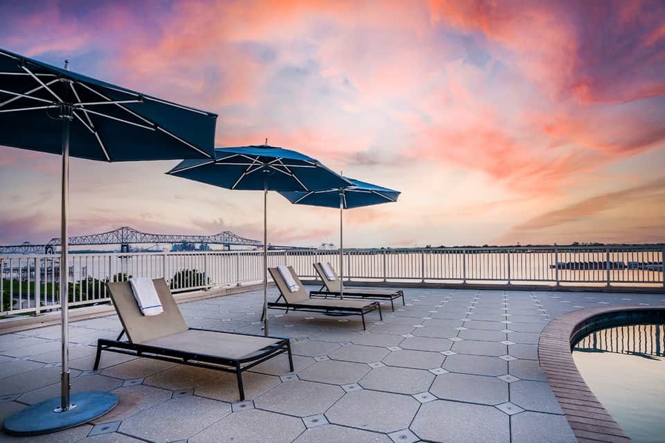 Sunset patio with blue umbrellas, lounge chairs, and bridge view over river