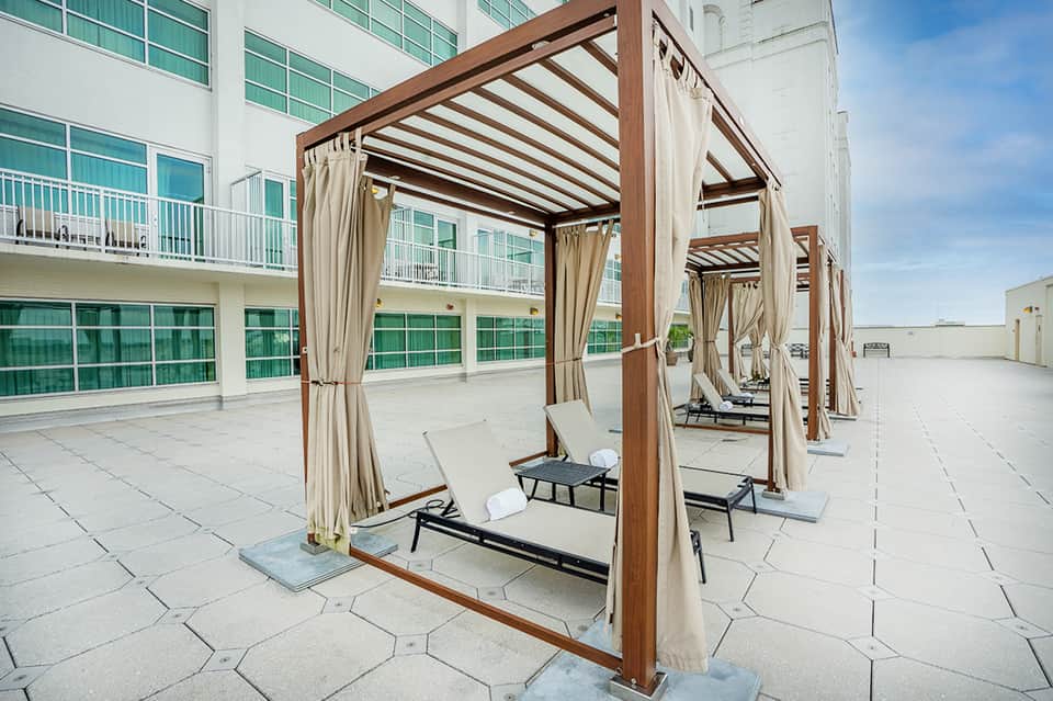 Rooftop lounge area with wooden pergolas, white curtains, and lounge chairs overlooking ocean