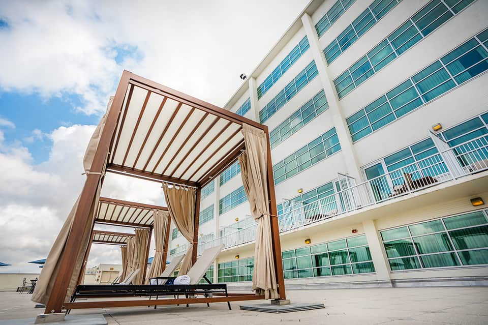 Modern wooden pergola structure on resort terrace with tall hotel building and cloud sky backdrop