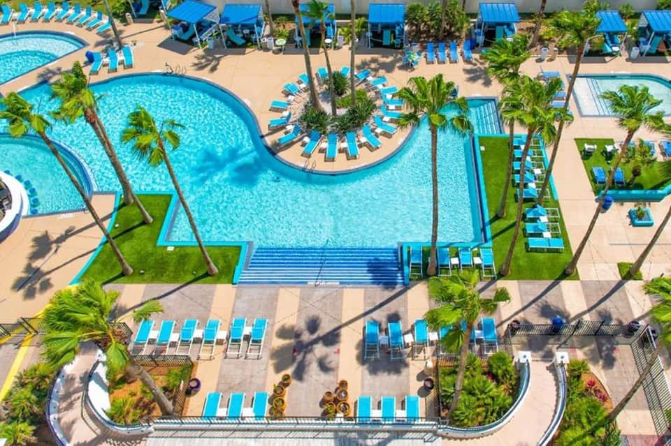 Aerial view of expansive resort pool complex with multiple pools, palm trees, and lounge chairs