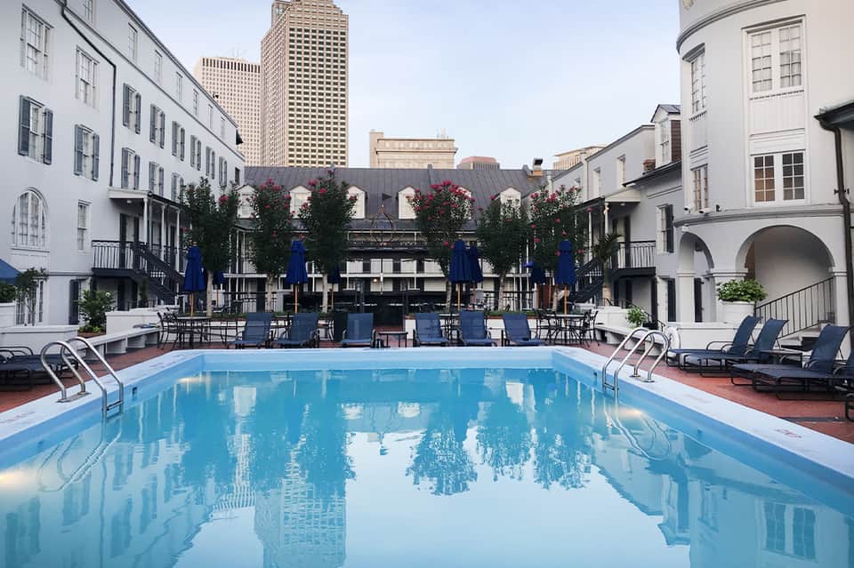 Urban resort pool in historic courtyard surrounded by classic colonial-style buildings and blue umbrellas