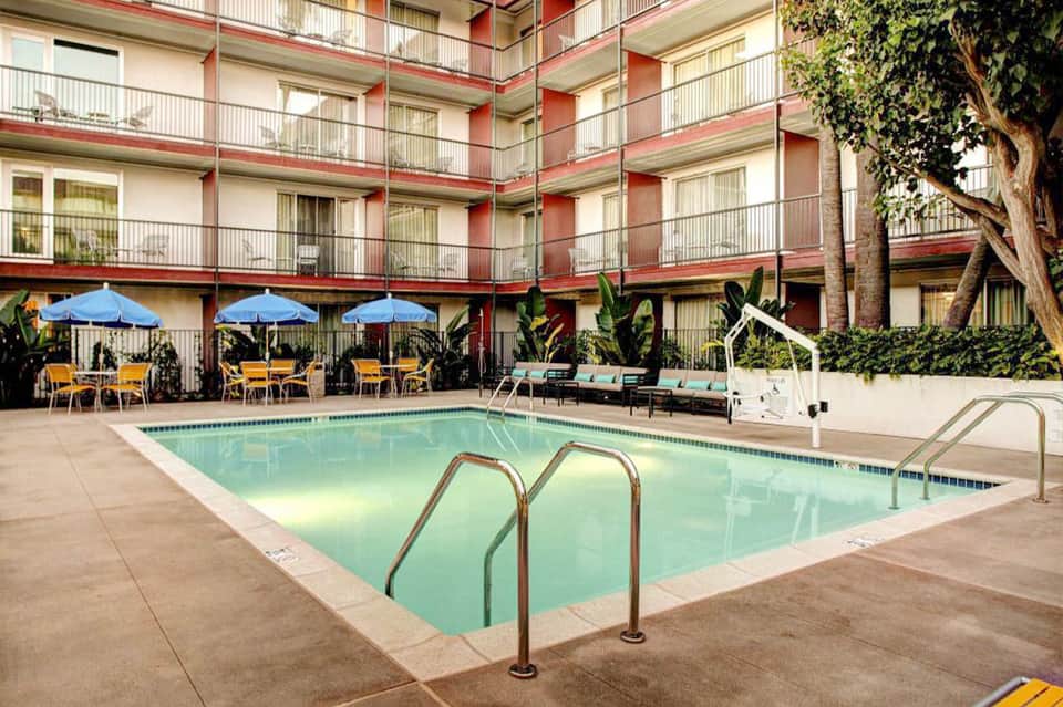Hotel courtyard with swimming pool, blue umbrellas, yellow chairs, and red-brick building facade